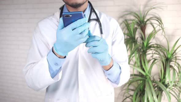 Doctor's Hand in Protective Gloves Using a Smartphone