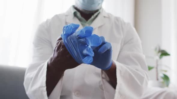 Mid section of male african american doctor wearing surgical gloves at home