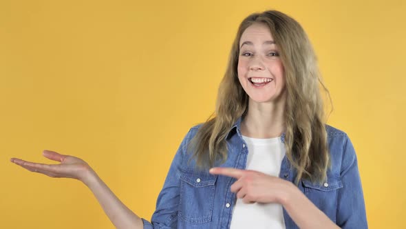 Portrait of Pretty Girl Showing Product at Side Yellow Background