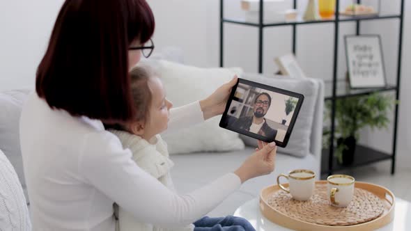 Mother and Her Daughter Sitting and Relaxing on Sofa at Home and Talking on Video Call with Smiling