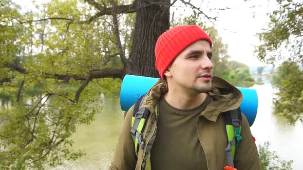 Young Tourist with a Backpack on His Back Stands in a Beautiful Forest.