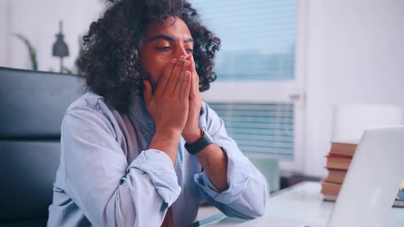 Tired Middle Eastern Man Clutches His Head While Sitting in His Office