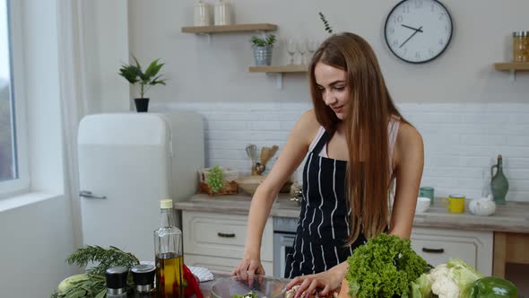 Vegan Girl Cooking Salad with Raw Vegetables While Looking on Mobile Phone for Online Recipe