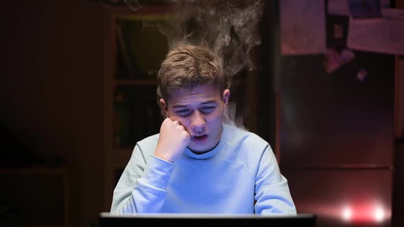 Smoke comes from a young guy who works at a computer in the middle of the night