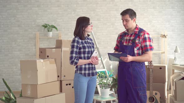 Loader in Uniform and Young Woman on the Background of Boxes for Moving New Home