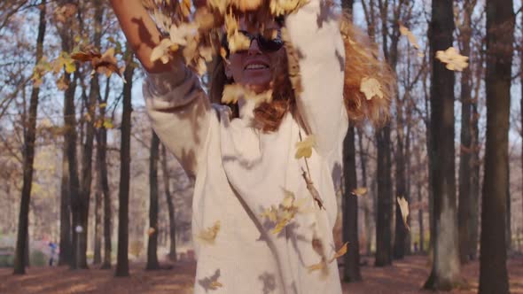 Girl Tossing Colorful Autumn Foliage Up in Air in Park.