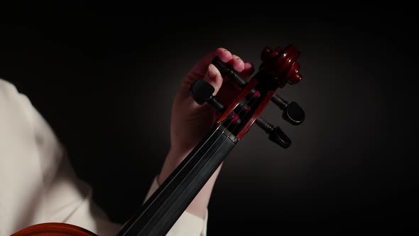 Violinist Woman Adjusts the Violin Twisting Pegs with Hand on a Dark Studio Background Closeup