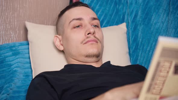 A Man is Reading a Book Lying on the Couch at Home Soft Focus