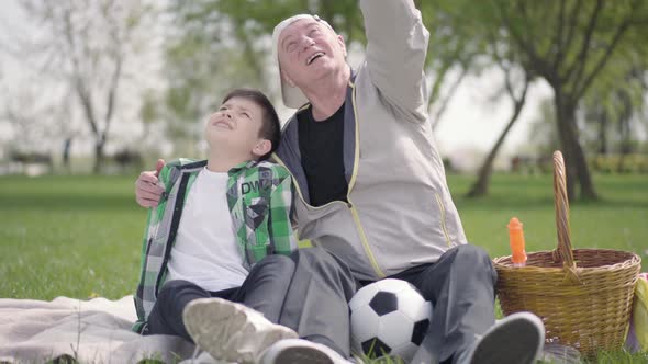 Old Man Sitting with His Grandson on the Blanket in the Park