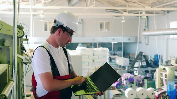 Factory Worker Using His Laptop To Monitor Plastic Bag Production Process