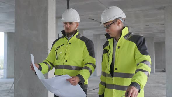 Two Engineer In Helmets With Tablet Device And Big Paper Drawings Discussing