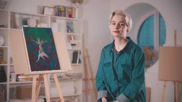 A Young Woman Artist with Short Blonde Hair Sitting in the Art Studio