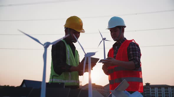 Asian engineer discussion about home solar cell farm and wind turbine model in construction site