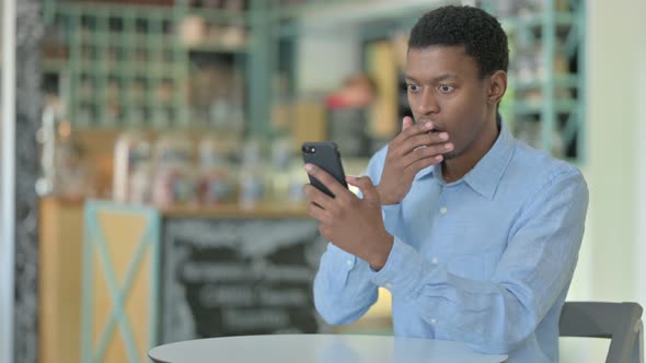 Upset African Businessman Having Loss on Smartphone in Cafe 