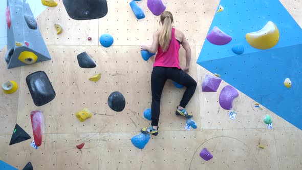 Woman bouldering up a wall in an indoor climbing center