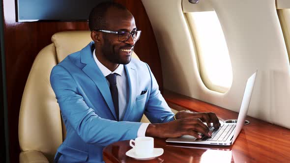 Businessman using laptop and drinking coffee on airplane
