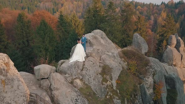 Newlyweds Stand on a High Slope of the Mountain