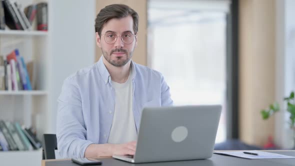 Attractive Man in Glasses with Laptop Looking at Camera