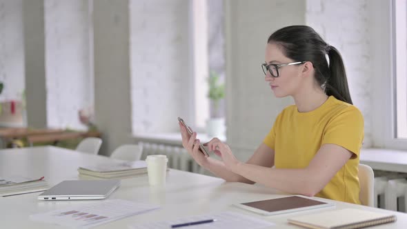 Focused Young Female Designer Using Smart Phone in Modern Office