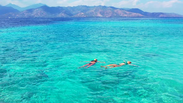 Girls relaxing lying floating on crystal emerald water of turquoise lagoon under sunlight of beautif