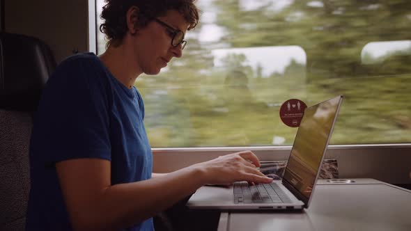 Woman in Glasses Working on a Laptop While Going By Train