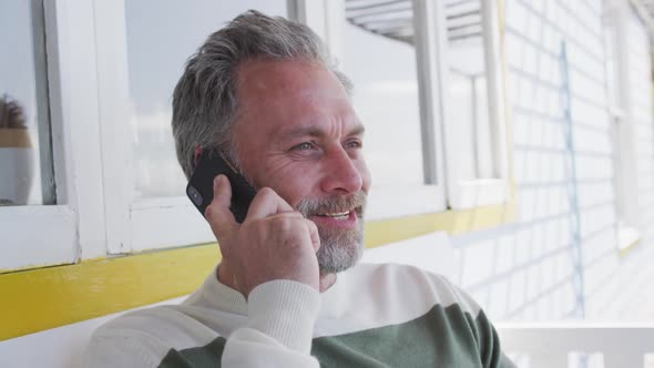 Happy caucasian mature man siting on the terrace and using smartphone