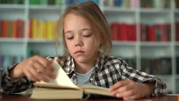 Closeup Front View of Serious Primary Child School Girl Flips Through Pages of Book and Reading Book
