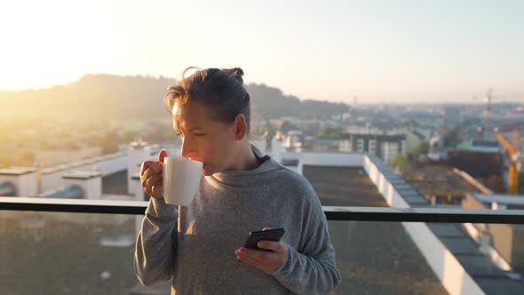 Woman Starts Her Day with a Cup of Tea or Coffee and Checking Emails in Her Smartphone on the