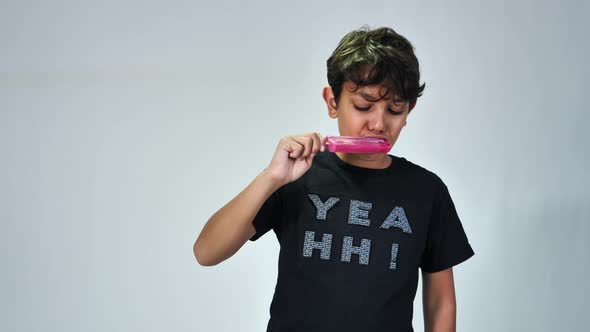 School boy eating popsicle ice cream isolated on grey background