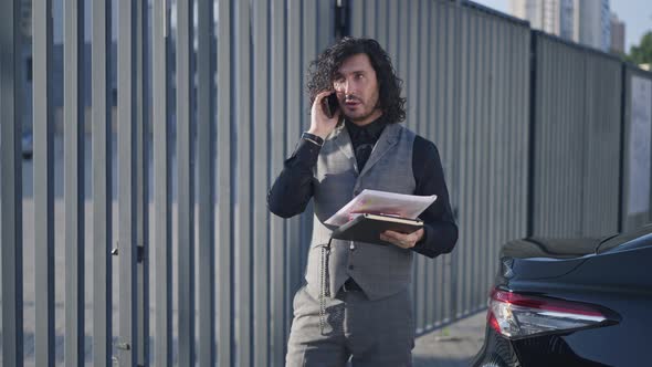 Busy Handsome Manager Standing in Urban City at Car with Paperwork Talking on Phone
