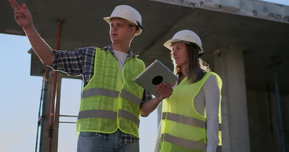 Professional Engineers in Safety Vests and Helmets Working with Digital Tablet and Blueprints.