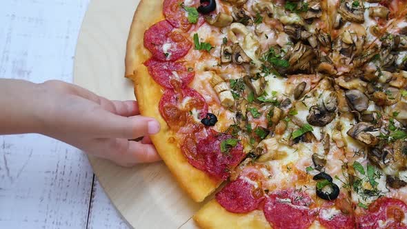 Pizza with Salami Close-up on a Wooden Table. The Child's Hand Takes a Piece of Pizza.