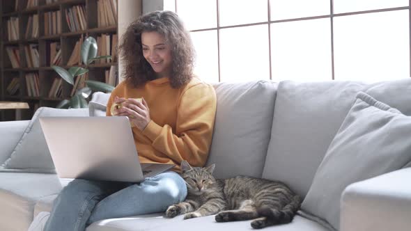 Happy Latin Girl Looking at Laptop Laughing Relaxing with Cat on Couch at Home