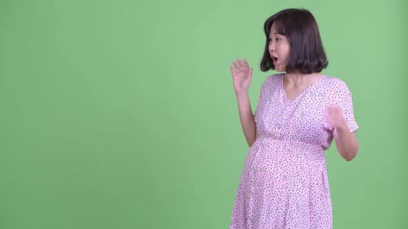 Happy Asian Pregnant Woman Touching Something and Looking Surprised