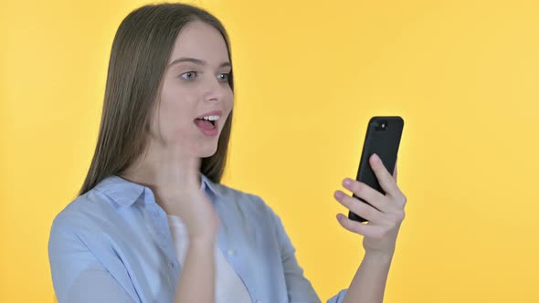 Casual Young Woman Celebrating on Smartphone, Yellow Background