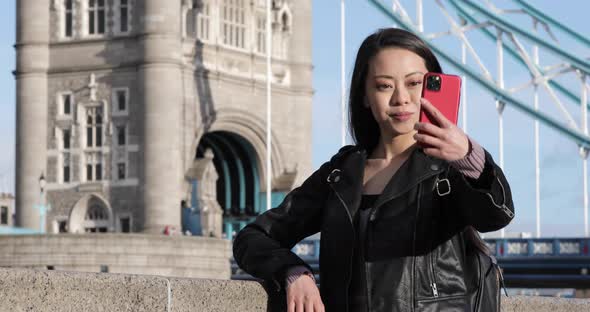 Chinese woman taking a selfie in London with Tower Bridge on background