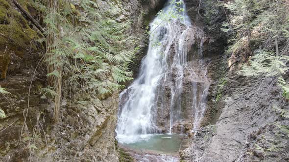 Margaret Falls flowing down a steep, rocky cliff in the lush forest of Herald Provincial Park in Bri