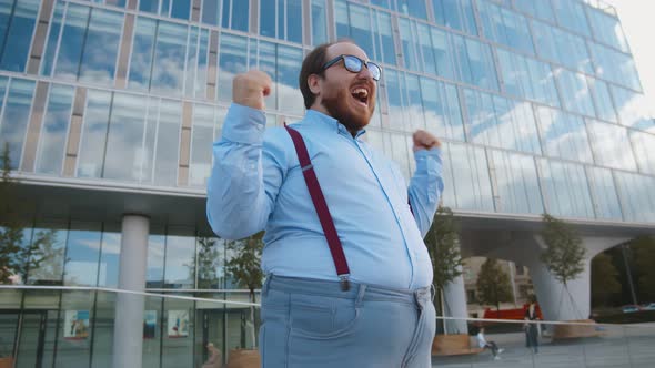 Portrait of Overweight Excited Businessman Doing Winner Gesture Standing Outdoors on Street