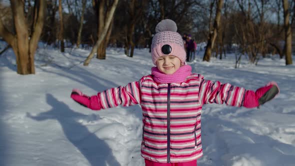Child Girl Looking at Camera Smiling Dancing Waving Hands on Snowy Road in Winter Park Outdoors