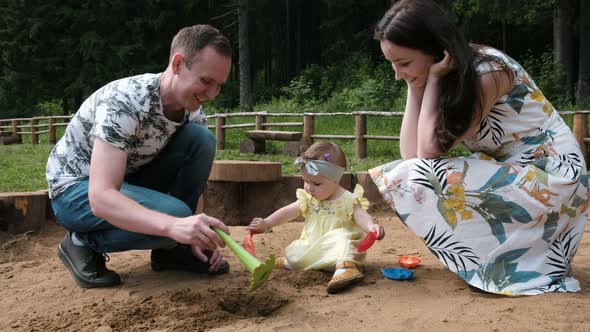 Happy Family with a Child Playing in the Sandbox - Father Builds Sand Figurines for His Daughter