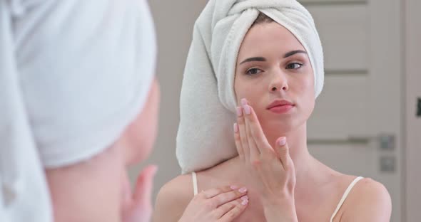 Young Female Stands in Front of the Mirror in Her Bathroom and Applies Cream on Her Face, Skin Care