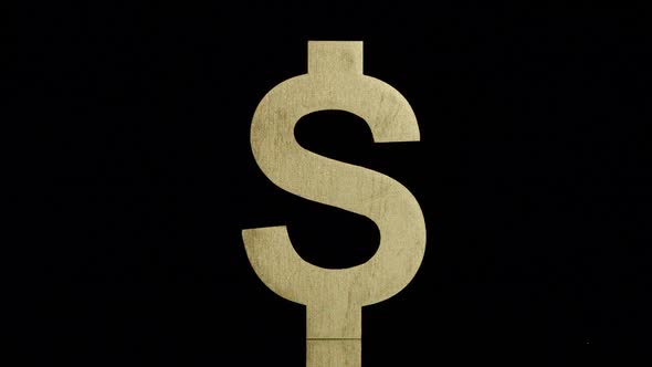 Golden US dollar symbol stands and falls back on a black background