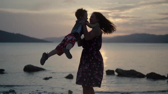 Mom with Son in Her Arms Rejoicing at Sunset By the Sea