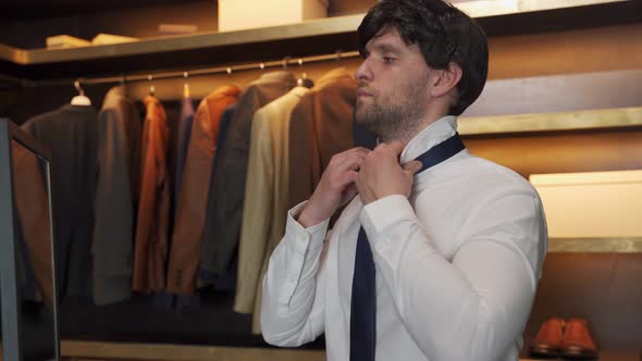 Man in a Shirt Gets Dressed and Adjusts a Blue Tie Around His Neck in the Dressing Room