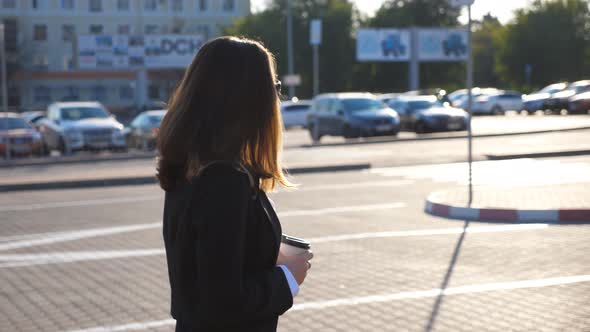 Profile of Young Businesswoman with Cup of Coffee Walking Near Auto Parking at Sunny Day. Business