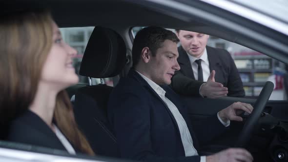 Side View of Handsome Young Caucasian Man Sitting in Car with Wife and Talking To Dealer