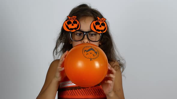 Happy Halloween. The girl inflates an orange balloon with a pumpkin pattern and enjoys the holiday. alt