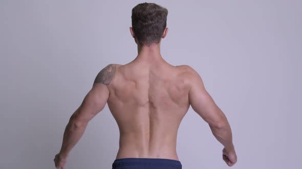 Rear View of Muscular Man Flexing Back Muscles and Biceps Shirtless