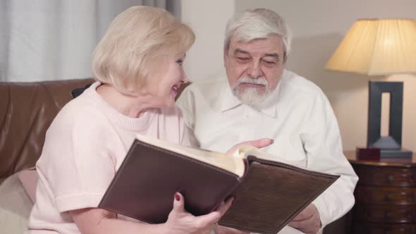 Portrait of Cheerful Caucasian Old Couple Watching Photos in Album and Talking, Happy Elderly