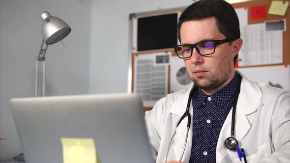 Male Doctor in White Coat with Stethoscope Working on His Laptop.